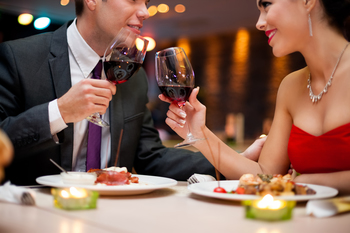 hands of couple toasting their wine glasses over a restaurant table during a romantic dinner.