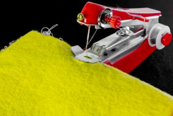 small red handheld sewing machine stitching on yellow fabric